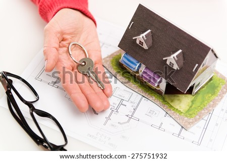 Closeup of woman hand giving residential house key to client. Concept of housing rent and sale. Shallow depth of field.