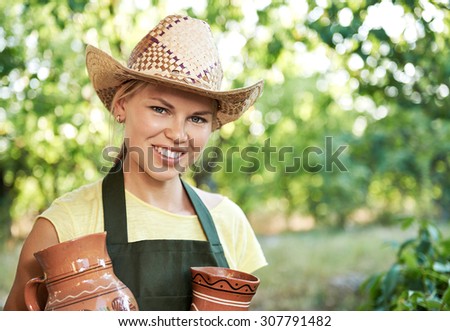 Smiling woman farmer holding old clay pitchers for beverage. Young winemaker with potteries of wine working in vineyard.