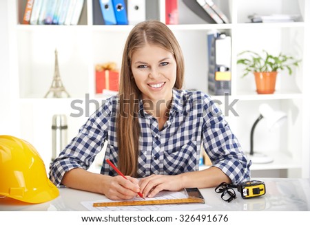 Cheerful woman architect estimating business plan of new project. Young female working on blueprint in her office.