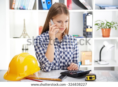 Pretty woman architect making estimate of new construction project. Young businesswoman with phone and draft in the office.