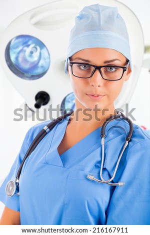 Young female surgeon with medical surgical lamp on background
