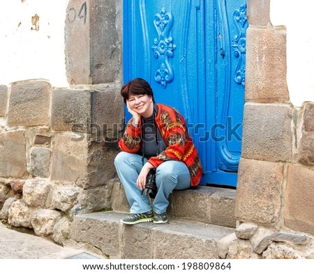 Young woman sitting on the steps of the house in the ancient city of Cusco in Sacred valley of the Incas, Peru