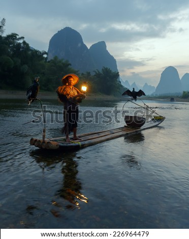 XINGPING, CHINA - OCTOBER 21, 2014: Cormorant fisherman stands on the ancient bamboo boat with a lighted lamp in his hands - The Li River, Xingping, China