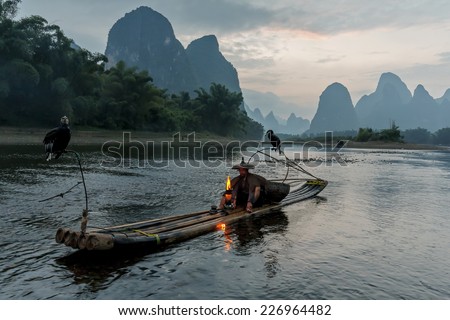 XINGPING, CHINA - OCTOBER 21, 2014: Cormorant fisherman sits on the ancient bamboo boat with a lighted lamp in his hands - The Li River, Xingping, China
