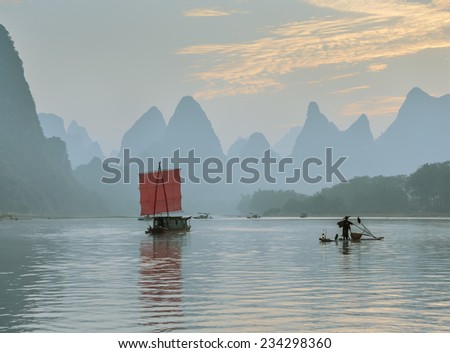XINGPING, CHINA - OCTOBER 23, 2014: Fisherman stands on traditional bamboo boats at sunrise (boat with a red sail in the background) - The Li River, Xingping, China