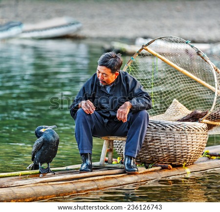 XINGPING, CHINA - OCTOBER 22, 2014: Cormorant fisherman talking to his bird after a successful fishing - The Li River, Xingping, China