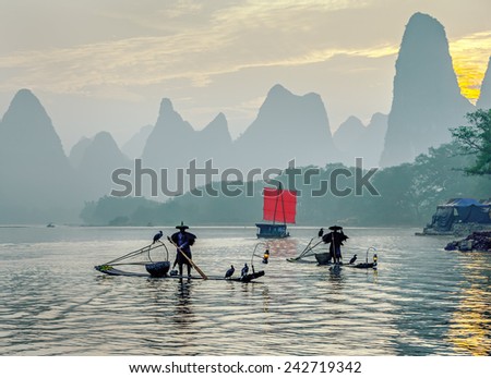 XINGPING, CHINA - OCTOBER 22, 2014: Fisherman stands on traditional bamboo boats at sunrise (boat with a red sail in the background) - Li River, Xingping, China