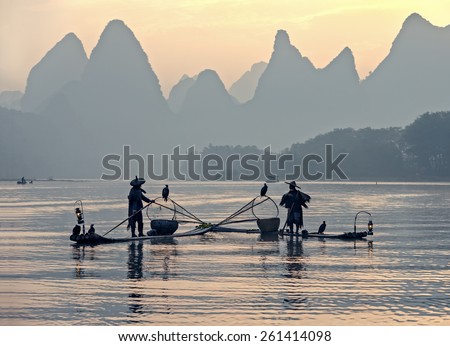 XINGPING, CHINA - OCTOBER 23, 2014: Fishermans stands on traditional bamboo boats at sunrise - The Li River, Xingping, China