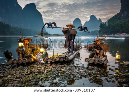 XINGPING, CHINA - OCTOBER 23, 2014: Cormorant fisherman on the ancient bamboo boat with a lighted lamps and cormorants - The Li River, Xingping, China
