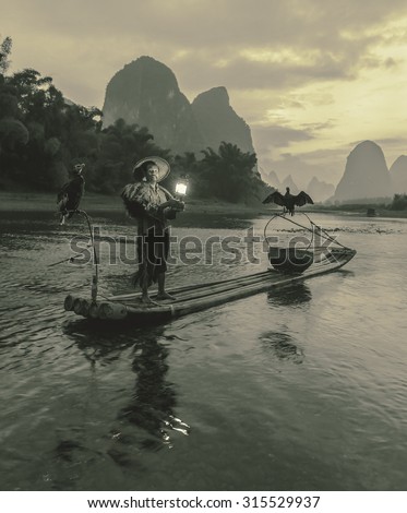XINGPING, CHINA - OCTOBER 21, 2014: Cormorant fisherman stands on the ancient bamboo boat with a lighted lamp in his hands - The Li River, Xingping, China (stylized retro)