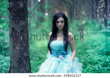 Beautiful girl in the lush turquoise dress standing in the woods.