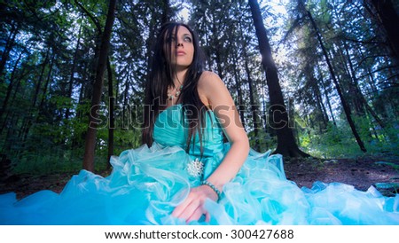 Beautiful woman in a blue dress sitting in a lush forest fairy.