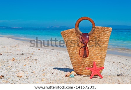 straw bag, sunglasses, starfish and shells by the shore