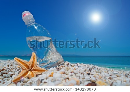bottle of water and sea star on white pebbles under a shining sun