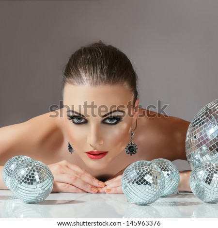 Close-up face of young woman with fashionable make-up and disco ball in hands