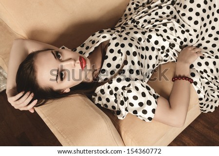 Retro style portrait of young beautiful woman lying on a vintage couch