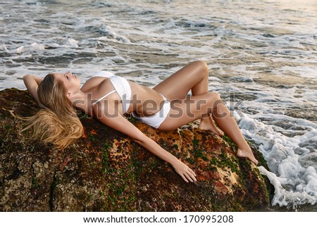 Young woman lying down on a stone rock at sea. Sunset time outdoor portrait made in India, State Goa