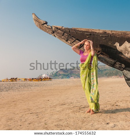 Young woman in traditional indian sari posing in front of old fisherman boat at india state goa