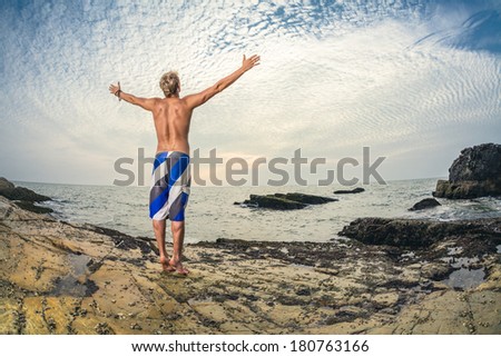 Athletic handsome man in swimming shorts posing in front of tropical sea
