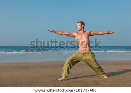 Young man doing yoga and meditating in warrior pose at sea beach