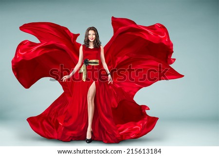 Sexy young motion woman in long red evening fluttering fashion dress flying over background
