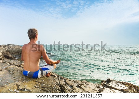 Man meditating in front of sea sitting in lotus position