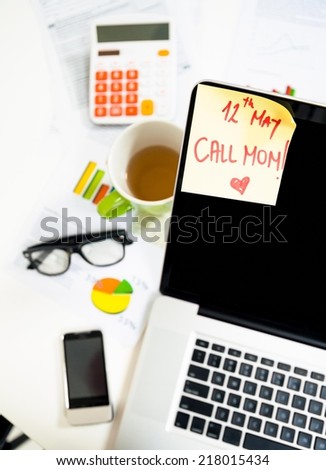 Laptop and a reminder on the monitor to call mom for Mother\'s Day.