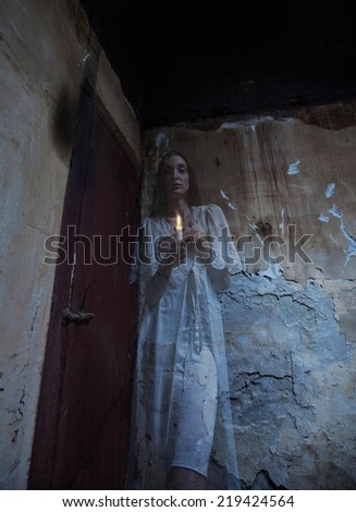 Scary woman standing in a dark hallway with lighten candle.