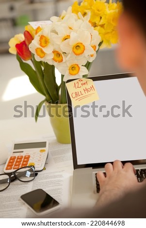 Man working on a laptop. Having reminder on his monitor to call mom for Mother\'s Day.
