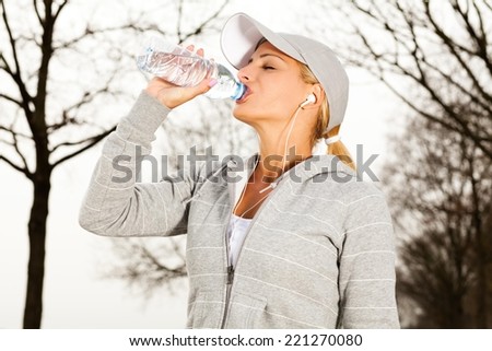 Young beautiful sport woman drinking water after running in nature.