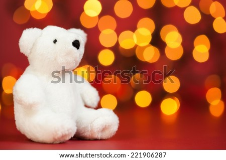 Small white teddy bear with the christmas lights in the background.
