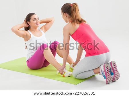 Young women doing sit-ups in a studio. Helping each other.