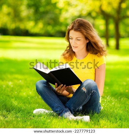 Beautiful girl in the park holding a book and day dreaming.