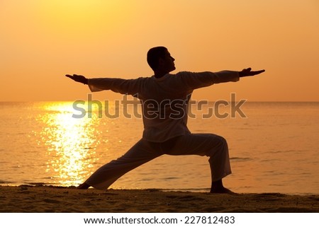 Young man practising yoga at the beach - warrior II pose.
