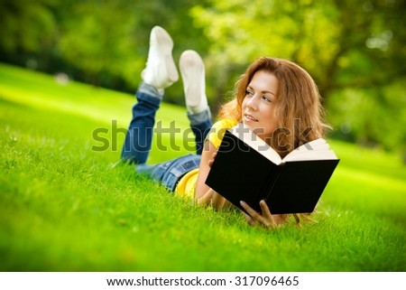 Beautiful girl in the park holding a book and day dreaming.
