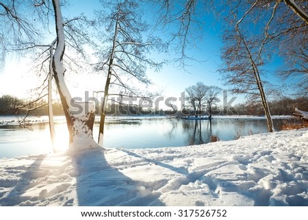 Winter scene in Belgium by the lake - sun reflection on the ice covered lake.
