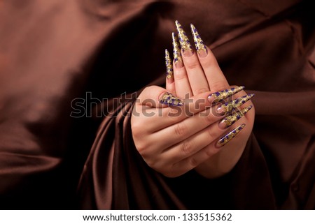 Hands with long fingernail and beautiful manicure over brown silk