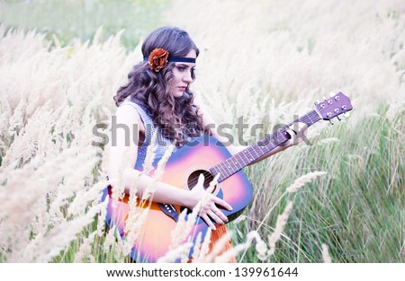 Attractive young woman dressed in vintage 1960\'s hippie style play on guitar at the meadow
