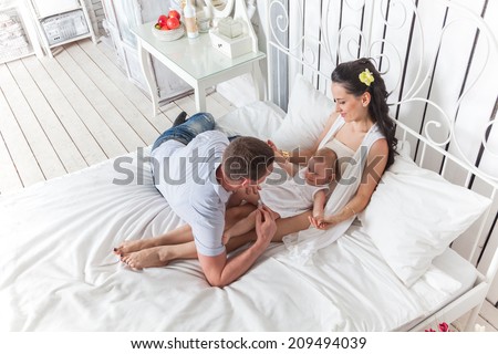 Good morning! Lovely family sitting together on the bed. Mother and father playing with his daughter.