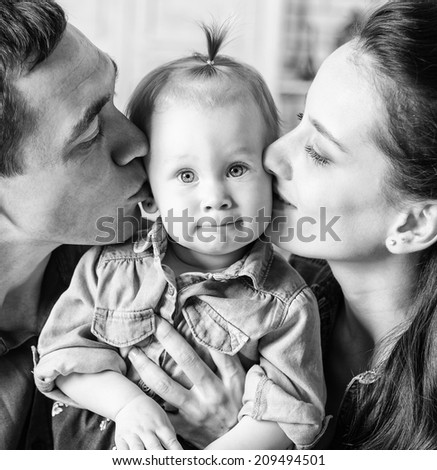 BW portrait of lovely family together at home. Mother and father kissing his year-old daughter