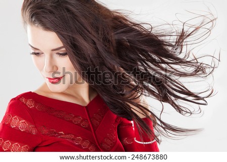 Fashion brunette woman with beauty long straight hair fluttering in the wind. Creative studio image over gray