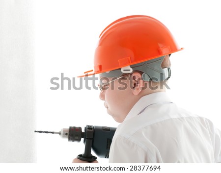 Teenager in protective helmet and spectacles drill the wall