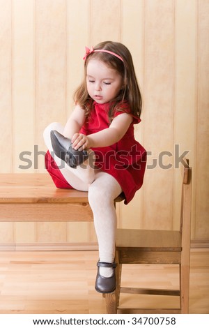 Little girl sitting on table and put on one\'s shoes