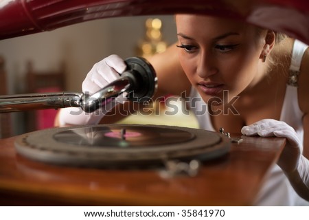Beautiful young woman in vintage interior start playing music on retro-style gramophone.