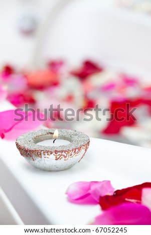 Spa treatment bathtub with candles and floating rose petals. Focus on candle