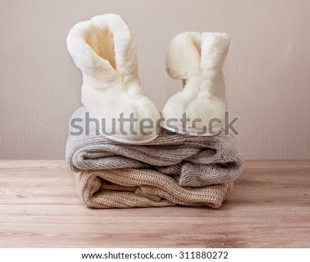 Pair of warm winter sheepskin slippers (alpaca)  on  pile of warm woolen clothes (Selective focus)