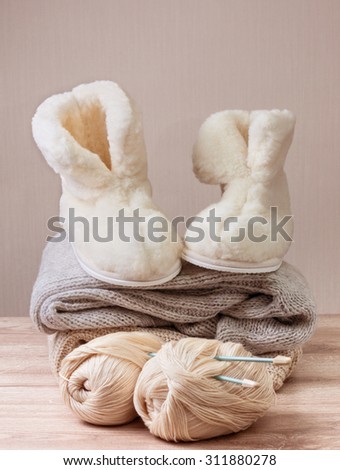 Pair of warm winter sheepskin slippers (alpaca), wool yarn , pile of warm woolen clothes (Selective focus)