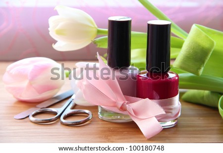 A set of manicure appliances: nail scissors, nail file and two shades of shiny nail polish with pretty tulips on the side