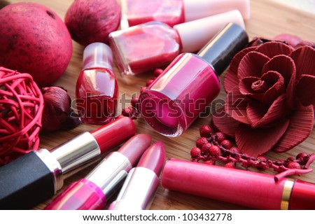 A collection of makeup: lipsticks, lip gloss and nail polishes decorated with red potpourri all in red and pink shades