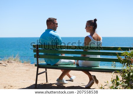 Back view of beautiful love couple sitting outdoors on a bench looking the  sea and sky in background - Stock Image - Everypixel